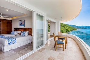 A bedroom with a bed, a bedside table, and a chair. There is a balcony with a table and chairs.
