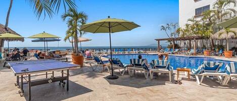 A poolside area with lounge chairs, umbrellas, and a ping pong table.