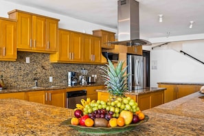A kitchen with granite countertops, wooden cabinets, stainless steel appliances, and a fruit bowl on the counter. - Elegant Multi-level Penthouse With Rooftop Jacuzzi, bay Views, Pool & Game Room (Puerto Vallarta)