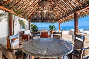 A covered outdoor seating area with a round table, chairs, and a view of the ocean. - Elegant Multi-level Penthouse With Rooftop Jacuzzi, bay Views, Pool & Game Room (Puerto Vallarta)