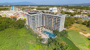 A high-rise hotel with multiple floors, a swimming pool, and a golf course in the background. - Enchanting & Modern Beach Retreat With Pool, Gym, & Breathtaking Balcony Views (Puerto Vallarta)
