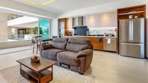 A modern living room with a sofa, a coffee table, and a kitchen area with a refrigerator and microwave. - Enchanting & Modern Beach Retreat With Pool, Gym, & Breathtaking Balcony Views (Puerto Vallarta)