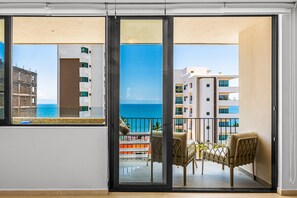 Un balcon avec vue sur l’océan, une table avec des chaises et un petit espace jardin.