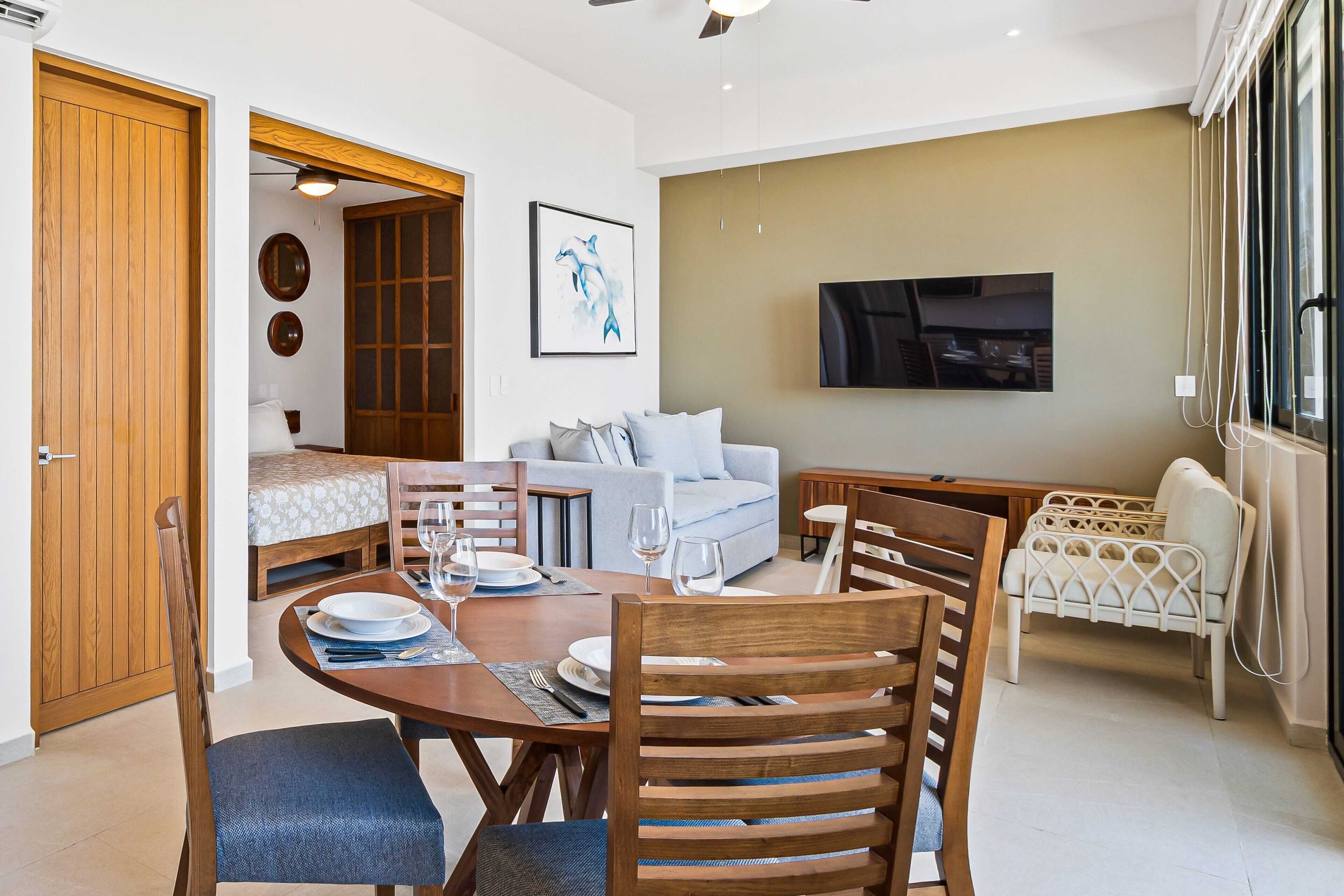 A modern living room with a dining area, a sofa, a TV, and a wooden door.