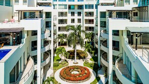 A multi-story hotel with balconies, a central courtyard with palm trees, and a circular flower bed. - Ocean-view Penthouse With Private Plunge Pool & Terrace, Resort Pool (Nuevo Nayarit)
