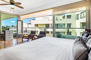 Ein modernes Hotelzimmer mit einem großen Bett, einem Balkon mit Sitzgelegenheit und Blick auf die Skyline.