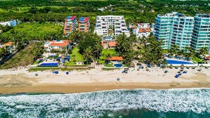 An aerial view of a coastal hotel with multiple buildings, a beach, and ocean waves. - Ocean-view Penthouse With Private Plunge Pool & Terrace, Resort Pool (Nuevo Nayarit)