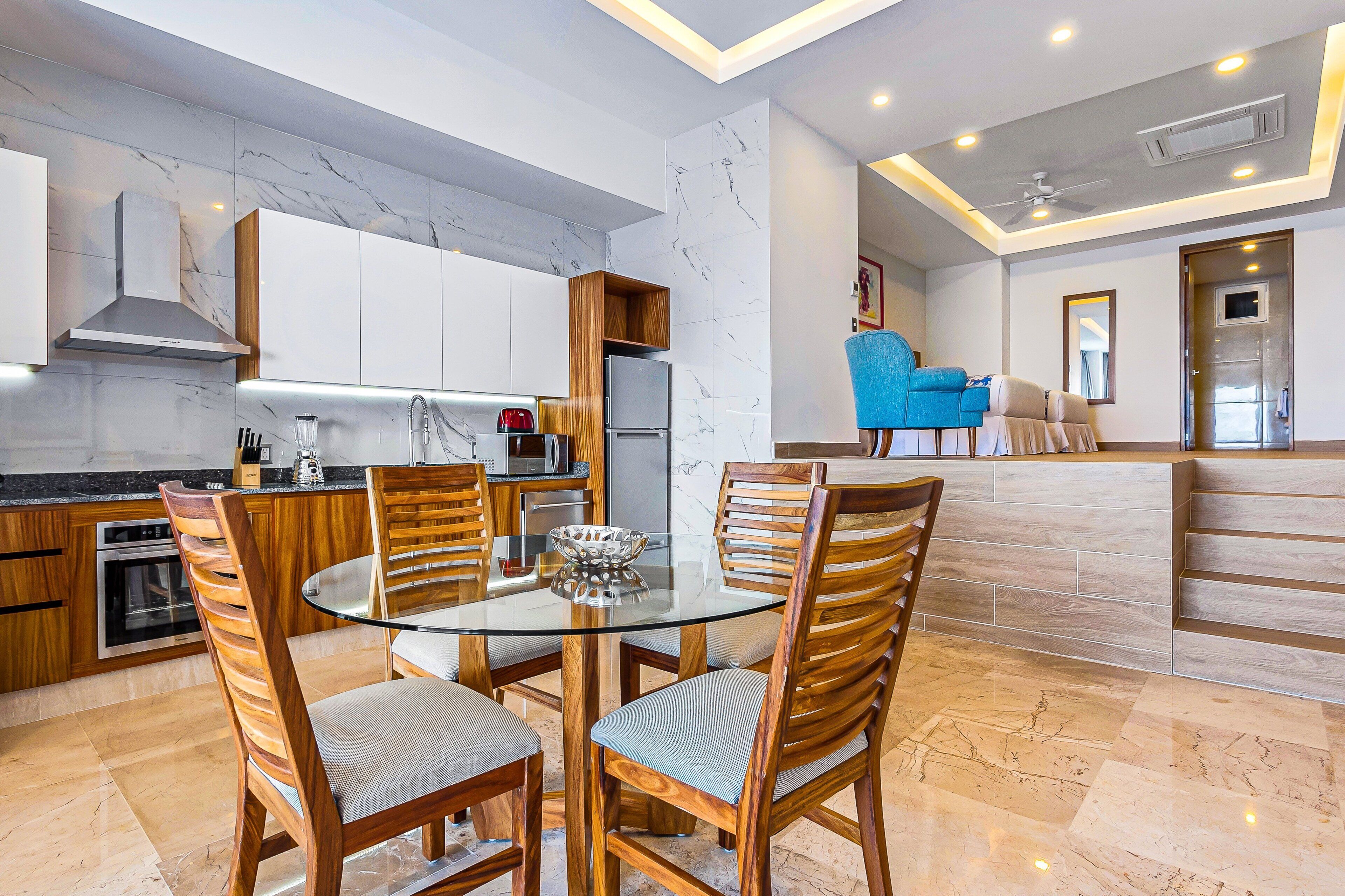 Une cuisine moderne avec des plans de travail en marbre, des meubles en bois et une table à manger en verre, assortie de chaises.
