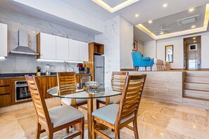 Cozinha moderna com bancadas de mármore, armários de madeira e mesa de jantar de vidro com cadeiras.