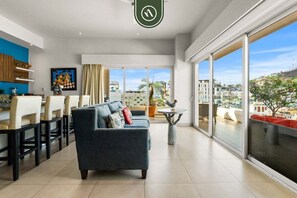 Ein modernes Wohnzimmer mit einer Couch, einem Essbereich und großen Schiebeglasüren zum Balkon mit Blick auf die Stadt.
