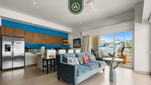 A modern living room with a blue sofa, a dining area, and a kitchen with wooden cabinets. - Amazing 2 BR Condo in Romantic Zone - Rooftop Pool (Puerto Vallarta)