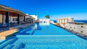 A swimming pool with a view of the ocean, lounge chairs, and a building with balconies. - Modern Condo With Rooftop Pool, Gym, & Private W/D (Puerto Vallarta)