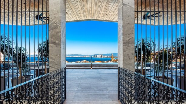 A view through a metal gate with a clear sky and a distant cityscape. - Modern Condo With Rooftop Pool, Gym, & Private W/D (Puerto Vallarta)