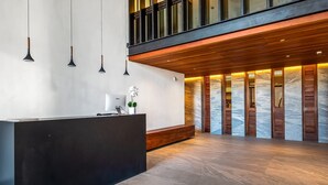 A reception area with a black reception desk, pendant lights, a wooden bench, and a marble wall with wooden shutters. - Modern Condo With Rooftop Pool, Gym, & Private W/D (Puerto Vallarta)