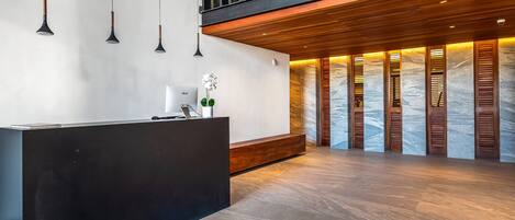 A reception area with a black reception desk, pendant lights, a wooden bench, and a marble wall with wooden shutters.