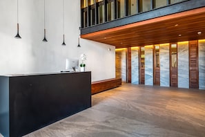 Zona de recepción con mostrador negro, lámparas colgantes, banca de madera y pared de mármol con contraventanas de madera.