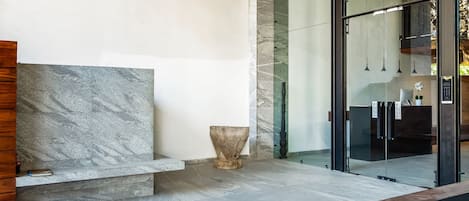 Una hall moderna con una panca in marmo, un vaso in pietra e l'ingresso di un ascensore in vetro.