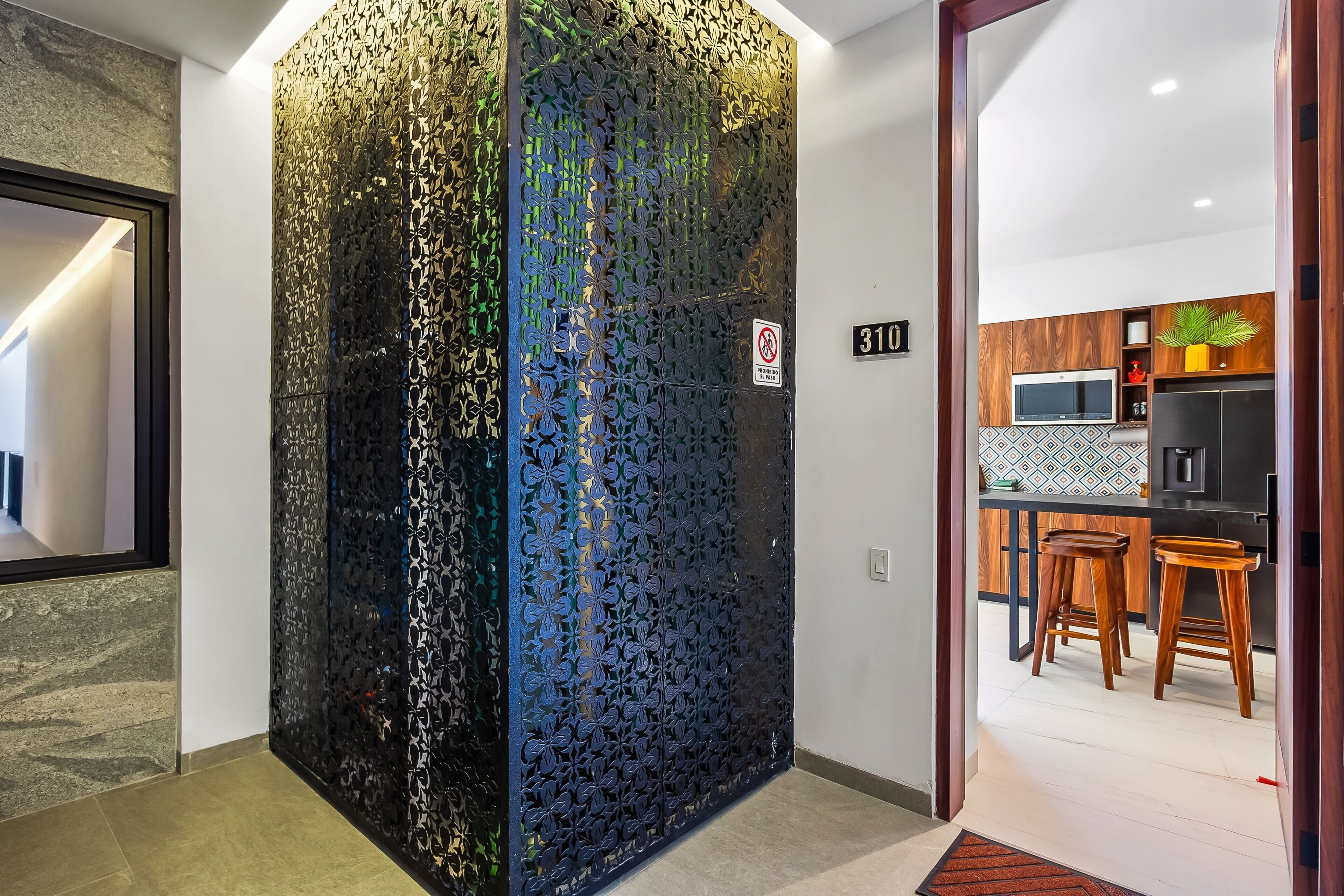 A modern interior with a decorative metal partition, a kitchen area with wooden stools, and a number sign '310' on the wall.