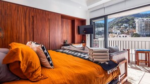 A bedroom with a bed, a TV, a balcony with a view of buildings. - Modern Condo With Rooftop Pool, Gym, & Private W/D (Puerto Vallarta)