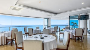 Een eetruimte met ronde tafels, stoelen en uitzicht op zee.