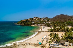 Una località costiera con spiaggia, case su una collina e palme.