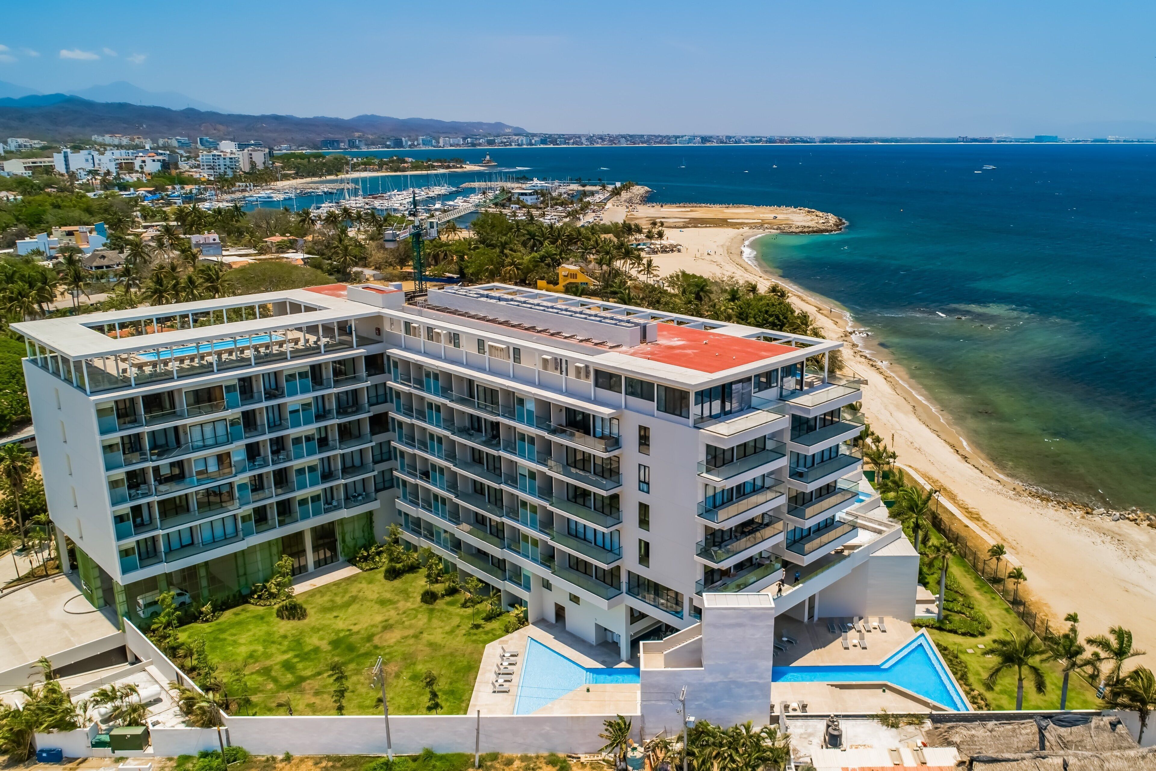 Un hôtel à plusieurs étages doté d’une piscine, situé près d’une plage et d’un port de plaisance.