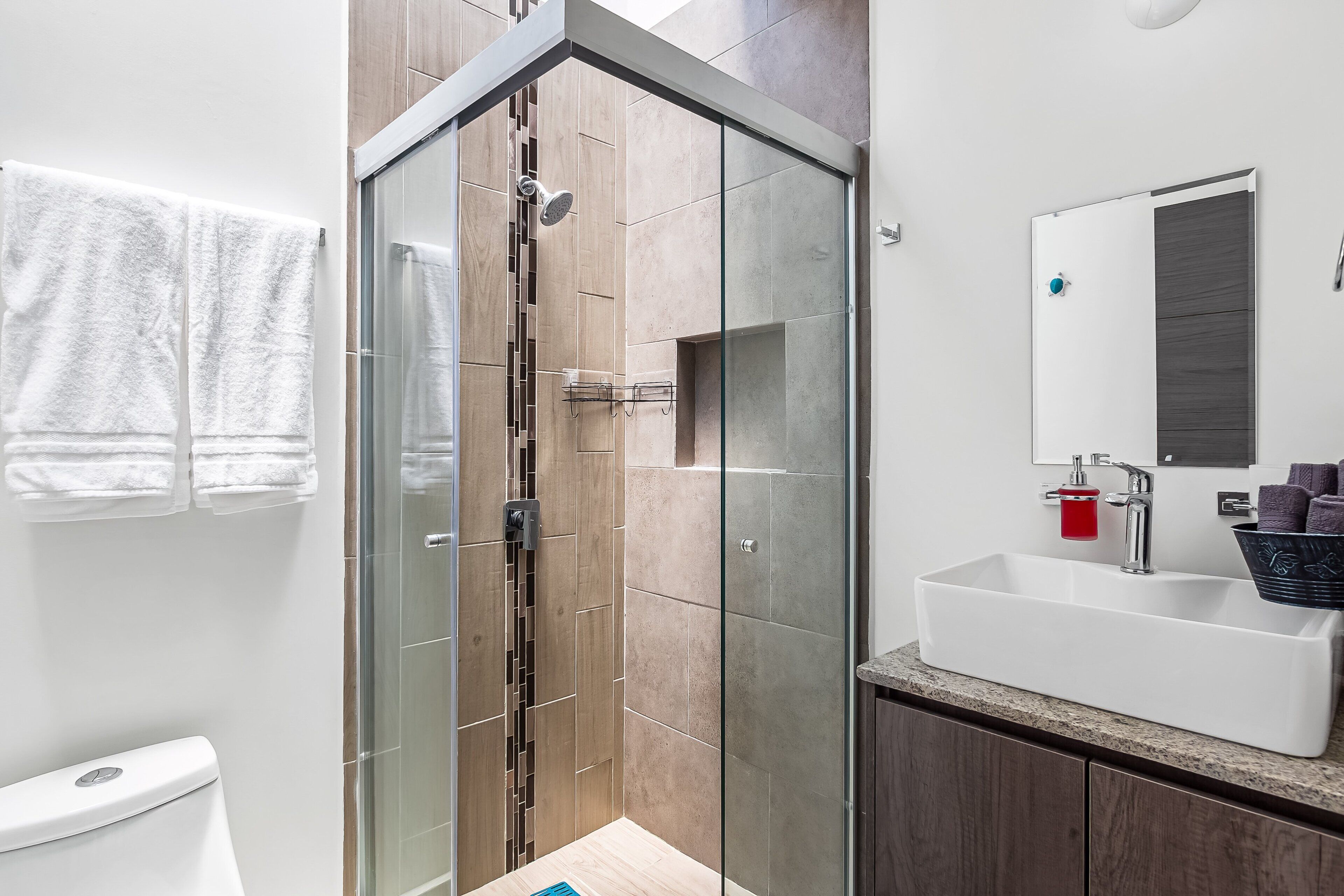 Un baño moderno con cabina de ducha de vidrio, un lavabo blanco y un inodoro.