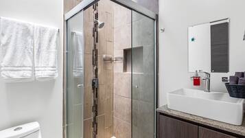 Un baño moderno con cabina de ducha de vidrio, un lavabo blanco y un inodoro.