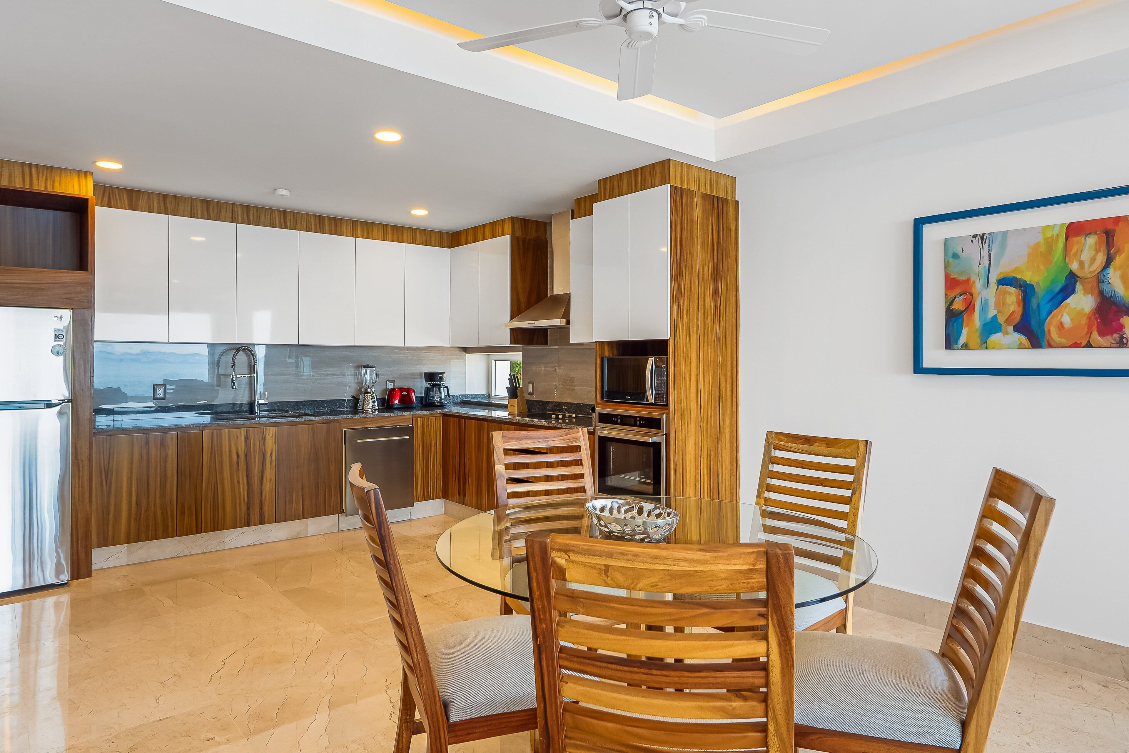 Una cucina moderna con mobili in legno, un tavolo da pranzo in vetro e una ventola a soffitto.