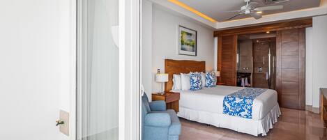 Habitación de hotel con cama, una silla, ventilador de techo y ventana grande.