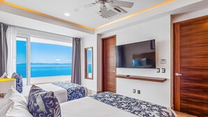 A hotel room with two beds, a TV, a ceiling fan, and a view of the sea. - Luxurious 6th-floor Condo With Pool, Oceanfront Balcony & Water View (Puerto Vallarta)