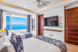 Ein Hotelzimmer mit zwei Betten, einem Fernseher, einem Deckenventilator und Blick aufs Meer.
