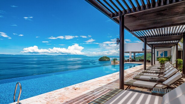An infinity pool with a clear view of the sea, lounge chairs, and a covered area with a pergola. - Luxurious 6th-floor Condo With Pool, Oceanfront Balcony & Water View (Puerto Vallarta)