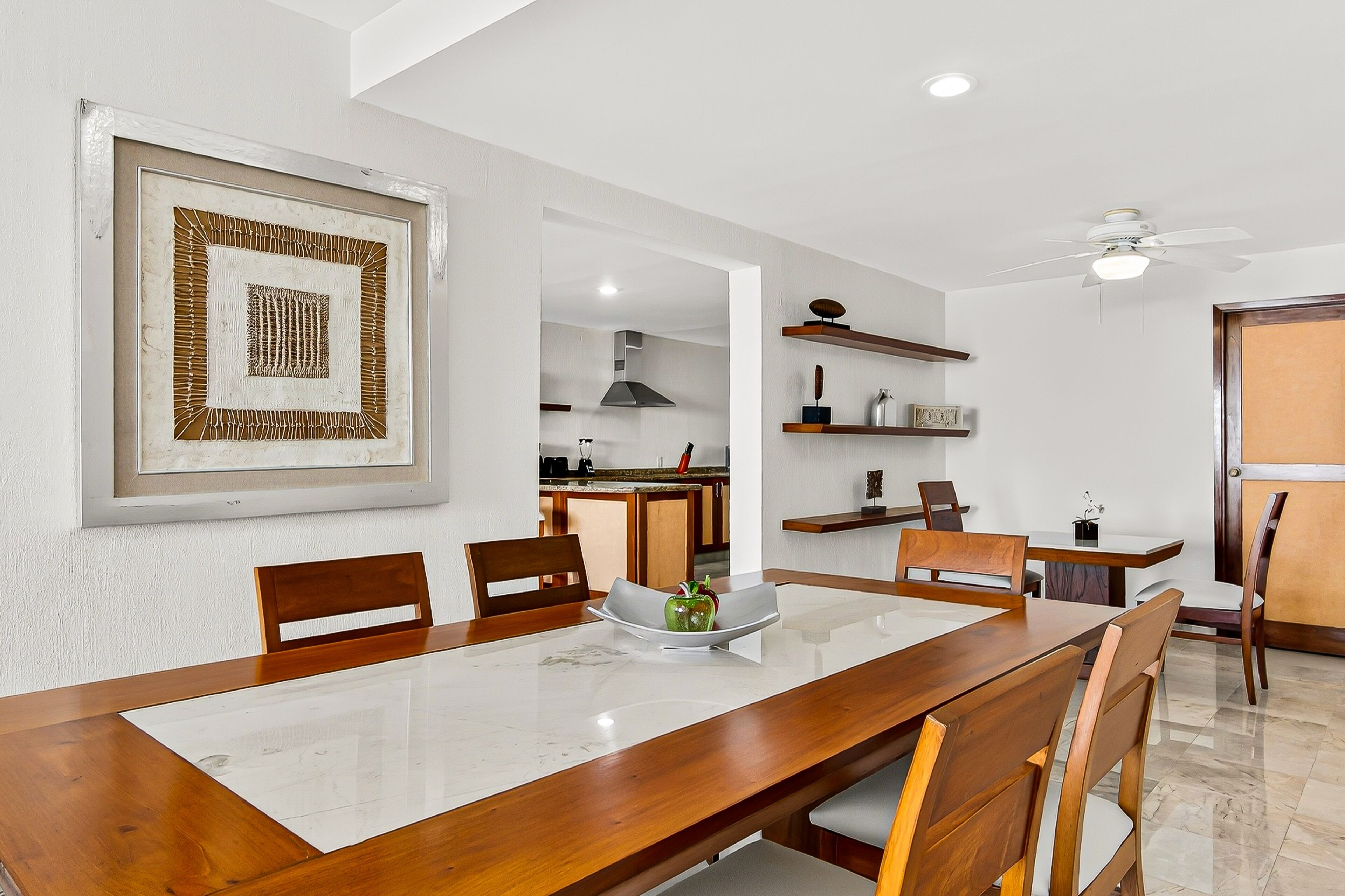 A dining area with a marble table, wooden chairs, and a framed artwork on the wall.