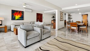 A spacious living room with a grey sofa, a dining area with wooden chairs and a table, and a ceiling fan. - Spacious Oceanview Suite With Heated Pool, hot tub & Terraces for Lounging (Puerto Vallarta)