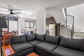 A modern living area with a sectional sofa, a dining table, chairs, a ceiling fan, and a kitchen in the background. - 2-story Home Near the Beach With Outdoor Pool, Patio, Washer/dryer, Streaming (Nuevo Nayarit)