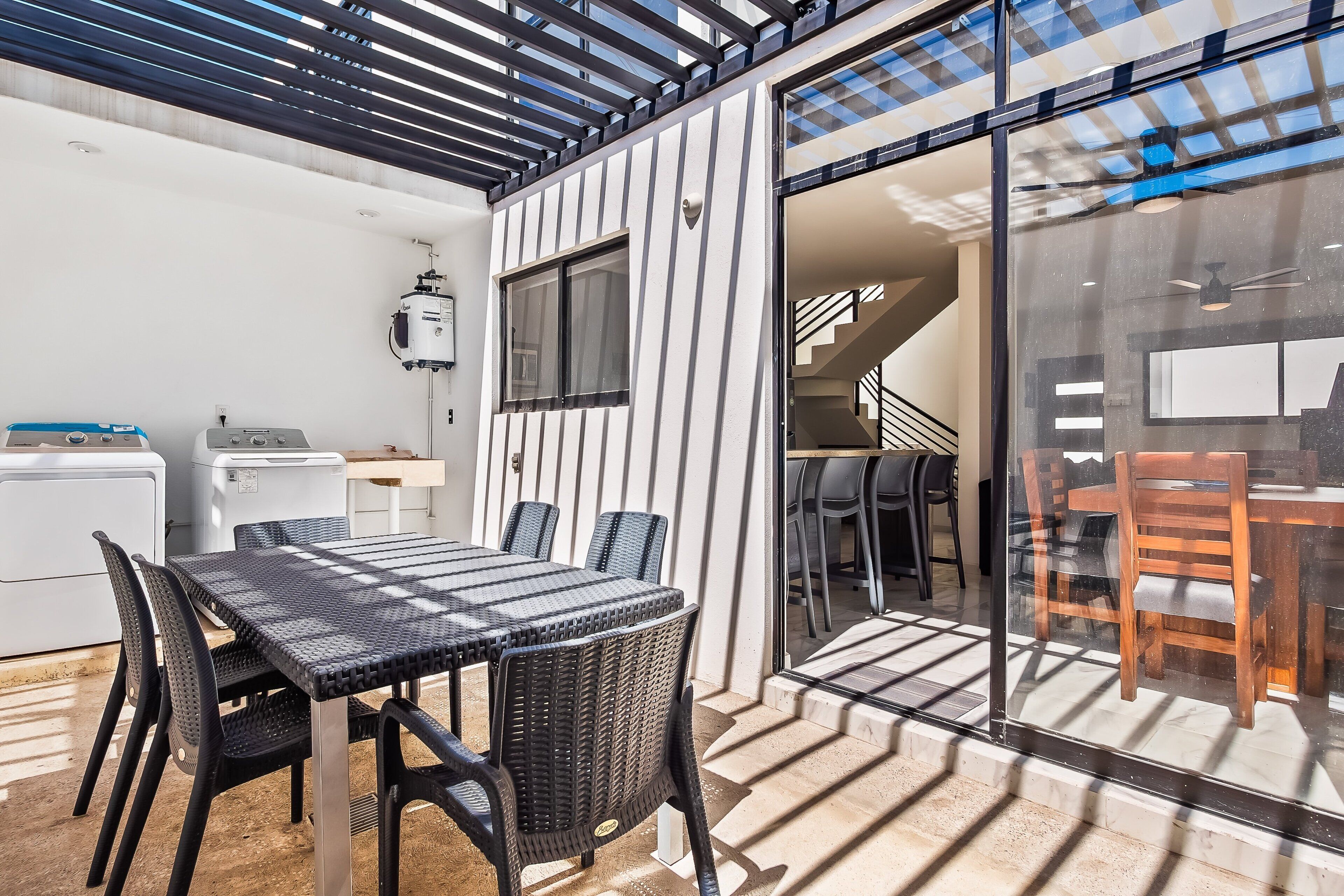 Una cocina moderna con lavadora incorporada, una zona de comedor con puerta de vidrio y una escalera que sube a un nivel superior.