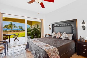 Ein Schlafzimmer mit einem großen Bett, einem Deckenventilator, einem Nachttisch und Blick auf eine Terrasse mit Gartenmöbeln und Pflanzen.