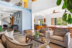 Uma sala de estar moderna com sofá, poltronas, mesa de centro e área de jantar com mesa e cadeiras de madeira.