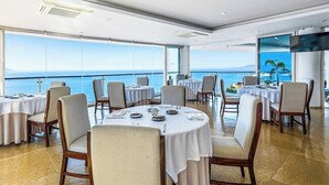 A dining area with round tables, chairs, and a large window offering a view of the sea. - Cozy Condo With Pool & AC - Family Base Near Beach & Activities, Shared hot tub (Puerto Vallarta)