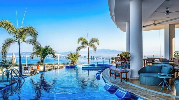 A pool with a view of the sea, palm trees, and a seating area with tables and chairs. - Cozy Condo With Pool & AC - Family Base Near Beach & Activities, Shared hot tub (Puerto Vallarta)