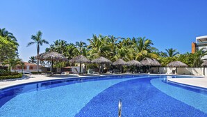 Una piscina con agua cristalina azul, rodeada de palmeras y sombrillas de paja.