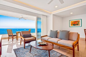 Uma sala de estar moderna com sofá, cadeiras, mesa de centro e vista para o oceano.