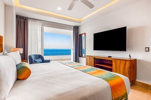 Quarto de hotel com uma cama grande, televisão de tela plana, armário de madeira e vista para o oceano.