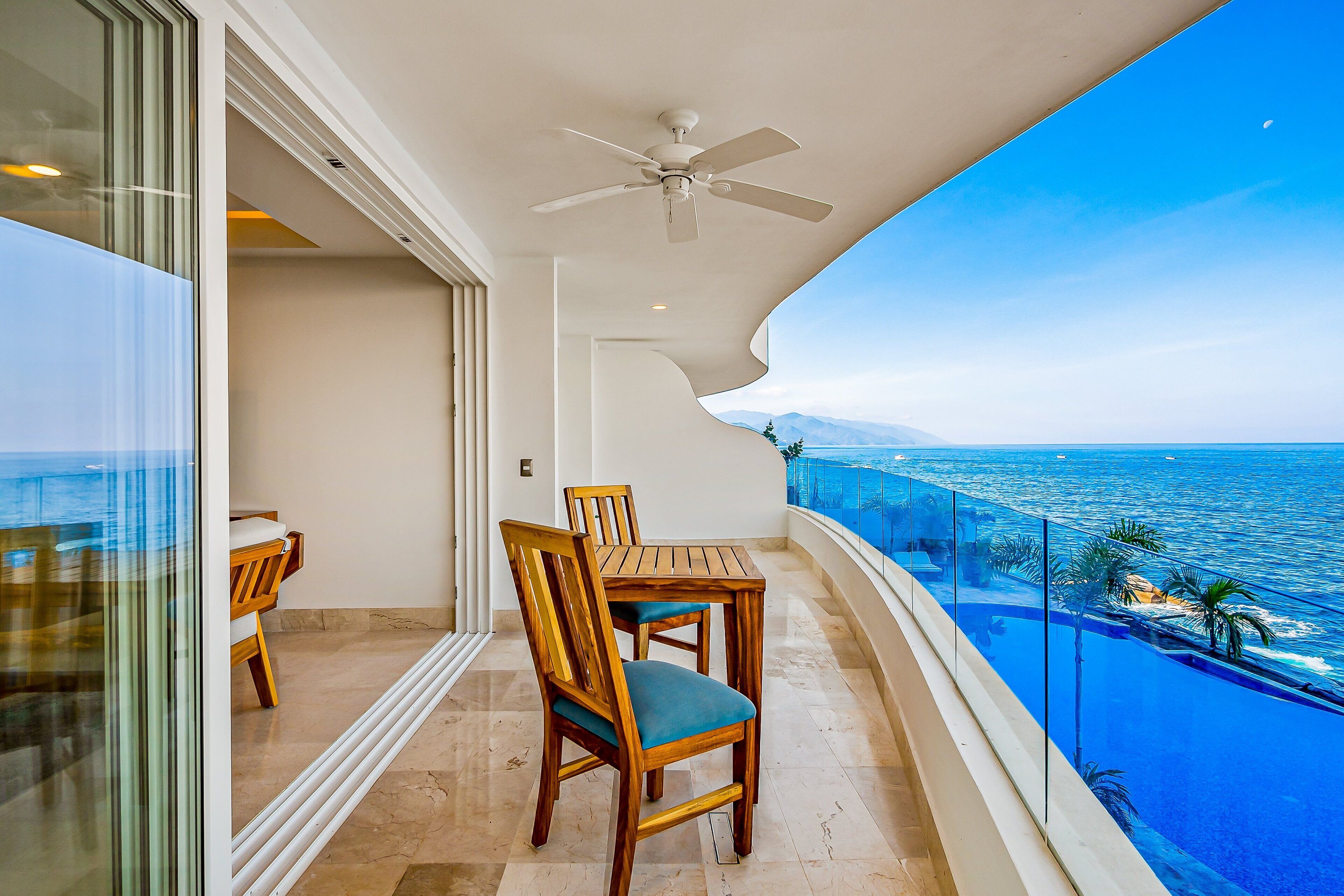 A balcony with a table and chairs, a ceiling fan, and a view of the ocean.
