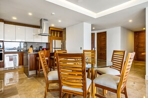 Uma cozinha moderna com armários brancos, uma coifa de aço inoxidável e uma mesa de jantar de vidro com cadeiras de madeira.