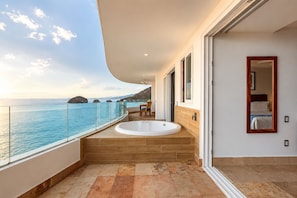 Un balcon avec un jacuzzi, une vue sur la mer et une chambre dotée d’un grand miroir.