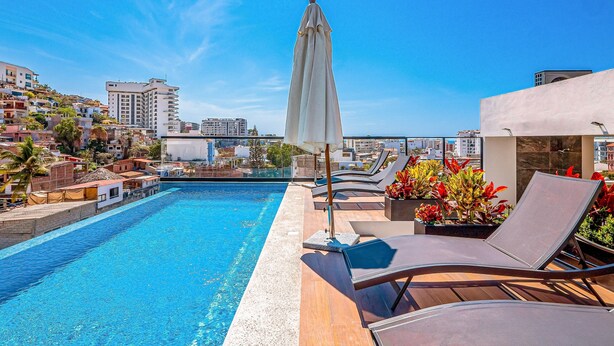 A rooftop pool with lounge chairs and an umbrella, surrounded by buildings and a clear sky. - 2nd-floor Condo With Heated Outdoor Pool, Grills, Balcony, W/d, AC (Puerto Vallarta)