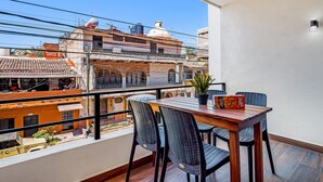 A balcony with a wooden table and chairs, a potted plant, and a view of buildings. - 2nd-floor Condo With Heated Outdoor Pool, Grills, Balcony, W/d, AC (Puerto Vallarta)