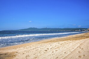 A beach with a clear sky, waves, and distant mountains. - Relaxing Condo With Pool, Balcony & Steps to Dining and Paseo Trail (Nuevo Nayarit)